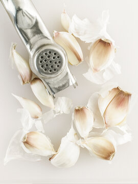 Close up of cloves of garlic and garlic crusher on white board
