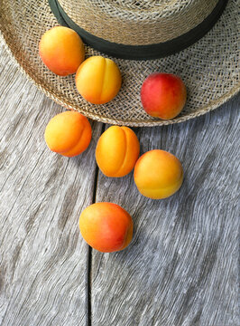 Fresh apricots resting on straw hat and wooden table