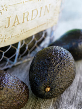 Close up of ripe avocados in wire basket and resting on old wooden table