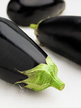 Close up of freshly picked aubergines resting on white tablecloth