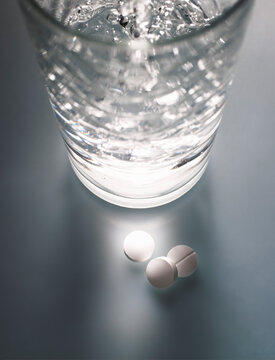 Water pouring into tall glass and pills on table
