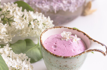 Berry milkshake, berry smoothie, copy space right, decorated with lilac flowers and green leaves. Healthy cocktail with vegan milk. Flat lay, spring cocktail in a jar on a white background