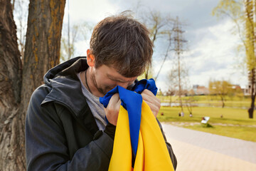 Sad young man going through a crisis holding the flag of Ukraine in the city street. The concept of freedom