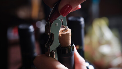 Bottle of red wine with corkscrew cap and open spiral is opened by woman