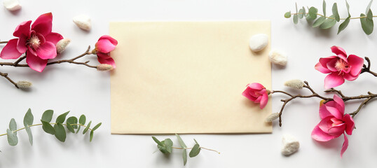 Pink magnolia flowers on twigs, fresh eucalyptus leaves. Blank pink card with grey envelope. Wood word love. Copy-space, place for greeting text. Chinese new year. Top view, off white background.