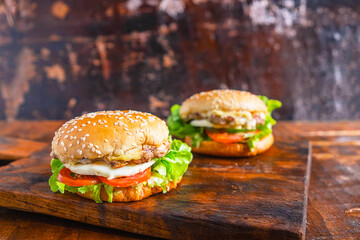 Close-up of delicious fresh home made burger with lettuce, cheese, onion and tomato on a rustic wooden plank on wooden table