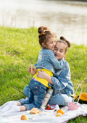 Two cute sisters girls on a picnic outside the city by the river. They communicate with each other and have a fun. Nature. Family. Vacation. Spring.