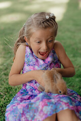 Little girl sitting on the green grass with rabbit. Cute child girl holding a bunny in her hands on Easter day.