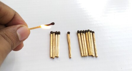 Hand with fire matchstick going to burn bunch of matchsticks on white table background surface with copy space among one keeping distance from others to protect others. Social distancing concept.