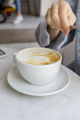 Cup of cappuccino with foam and female hand.