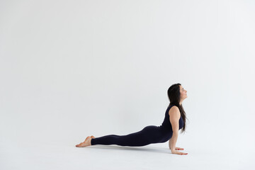 a beautiful young girl with dark hair stands in the Bhujangasana pose on a white background. Yoga class