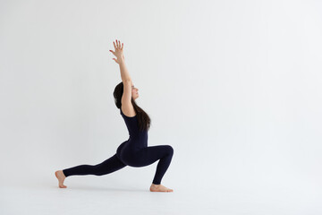 a beautiful young girl with dark hair stands in the pose of Virabhadrasana 1 on a white background. Yoga class