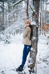 beautiful young woman in a snowy winter forest. girl in a brown sweater and hat. walk in the winter forest and be very happy. snow-covered trees. stylish clothes
