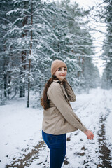beautiful young woman in a snowy winter forest. girl in a brown sweater and hat. walk in the winter forest and be very happy. snow-covered trees. stylish clothes
