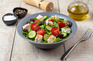 Fresh vegan salad from green leaves mix, vegetables, cheese, spices, olive oil and balsamic. Spring salad, healthy concept.  Wooden background