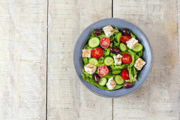 Green vegan salad from vegetables and green leaves mix, cheese, tomatoes and cucumber. Concept for a tasty and healthy meal. Top view. Copy space