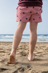 Photo of male legs wearing a swim suit while walking barefoot at the seaside of the beach in summer.