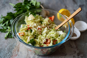 Vegetarian food. Salad of fresh vegetables: cabbage, tomatoes, onions, parsley in a glass bowl on a gray background. Close-up.