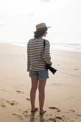 Photo of a young and attractive woman with a photo camera wearing summer clothes at the beach. Photography, holidays, travel. 