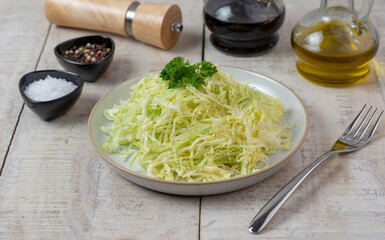 Shredded cabbage in plate on wooden background. Vegetarian healthy food with olive oil and balsamic and spices. Top view