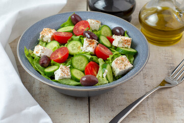 Fresh vegan salad from green leaves mix, vegetables, cheese, spices, olive oil and balsamic. Spring salad, healthy concept.  Wooden background