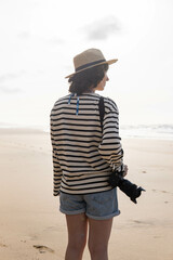Photo of a young and attractive woman with a photo camera wearing summer clothes at the beach. Photography, holidays, travel. 