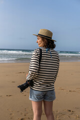 Photo of a young and attractive woman with a photo camera wearing summer clothes at the beach. Photography, holidays, travel. 