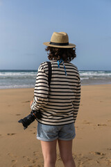 Photo of a young and attractive woman with a photo camera wearing summer clothes at the beach. Photography, holidays, travel. 
