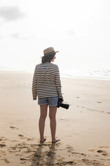 Photo of a young and attractive woman with a photo camera wearing summer clothes at the beach. Photography, holidays, travel. 