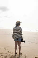 Photo of a young and attractive woman with a photo camera wearing summer clothes at the beach. Photography, holidays, travel. 