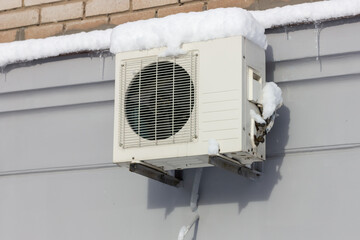 Snow-covered air conditioner on the wall of the house. Equipment icing.