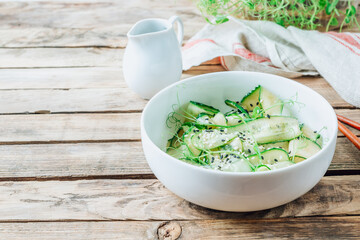 Salad of sliced cucumbers with herbs and sesame seeds in a white bowl