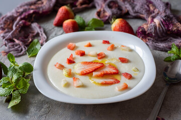 Breakfast for the whole family: semolina porridge with milk with strawberry slices and butter in a beautiful plate on a gray background. Porridge for children. Close-up.