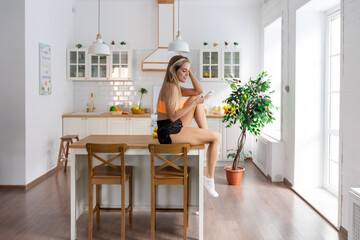 Young woman in sportswear taking a selfie while sitting on the kitchen table.