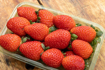 Red ripe strawberries in clear plastic tray, on wooden table