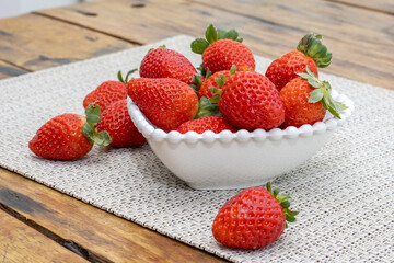 Delicious ripe fresh strawberries in a white bowl on a wooden table background