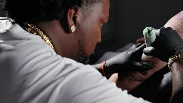 Professional African American tattoo artist makes a tattoo on client arm. High quality 4k footage.