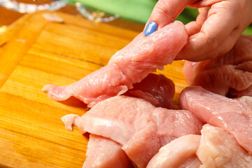 Female hands cut chicken fillet with a knife on a wooden board in the kitchen.