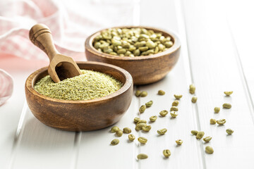 Ground green coffee in a wooden bowl and unroasted coffee beans.