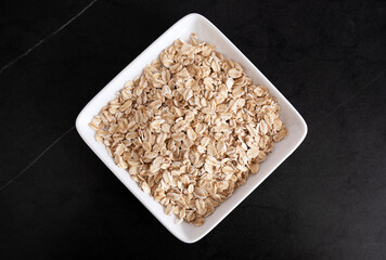 Oat flakes in a white plate on a black background, side view