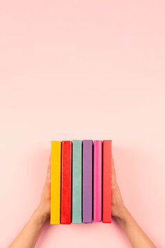 Female hands holding pile of books over pastel pink background. Education, self-learning, hobby, relax time at home