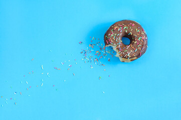 Bitten donut with chocolate icing and colored sugar decoration on a blue background. Top view, copy...