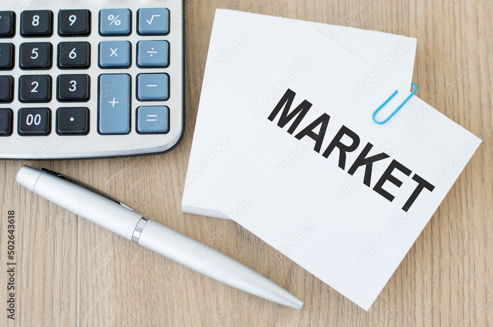 Poster market text on a card clip to sheets of paper for notes on a wooden table next to a calculator and p