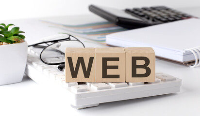 WEB s written on a wooden cube on keyboard with office tools