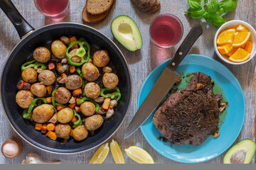 Dinner table with various snacks in the concept of homemade food, vegetables, herbs, fried steak in a pan, new potatoes