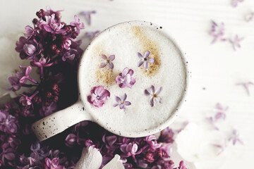 Delicious coffee with lilac petals and lilac branch on rustic white wooden background flat lay. Happy mothers day. Good morning. Hello spring. Space for text