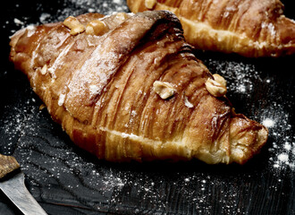 baked croissant on a wooden board and sprinkled with powdered sugar, black table. Appetizing pastries for breakfast