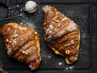 baked croissant on a wooden board and sprinkled with powdered sugar, black table. Appetizing pastries for breakfast