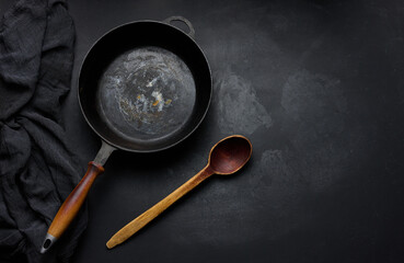 Empty round cast iron frying pan with wooden handle on black table, top view