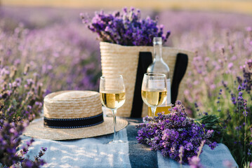 Two glasses with white wine and bottle on a background of a lavender field. Straw hat and basket...